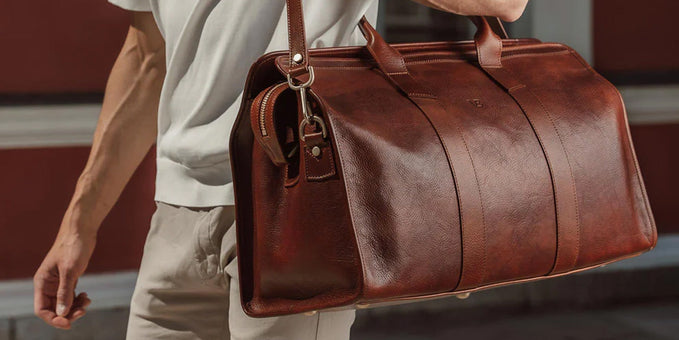 Man carrying a brown full-grain leather travel duffel that has darkened with years of use.
