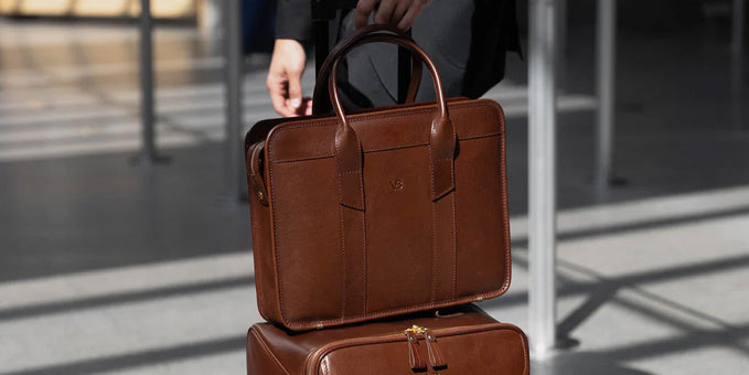 Brown leather Von Baer briefcase resting on a matching leather carry-on in an airport.