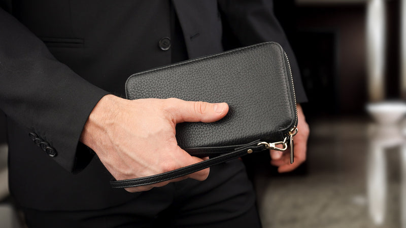 Von Baer origin luxury RFID men’s leather wallet in black with wristlet, held by a male model.