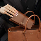 Von Baer Allure large cognac tan full-grain leather accordion wallet rest on a matching Estelle small tote bag, with a manicured hand resting on the wallet and a black blazer in a luxury lifestyle setting.