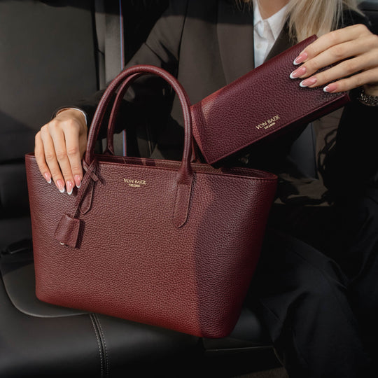 Von Baer Allure large burgundy full-grain leather accordion wallet with RFID protection paired with an Estelle small tote bag, shown in a premium car interior lifestyle setting.