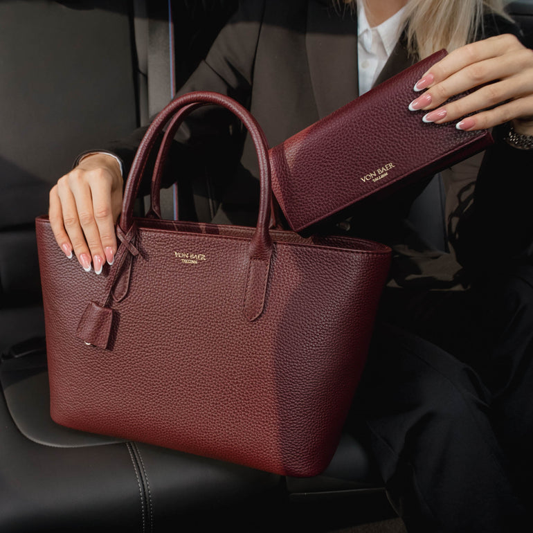 Von Baer Allure large burgundy full-grain leather accordion wallet with RFID protection paired with an Estelle small tote bag, shown in a premium car interior lifestyle setting.