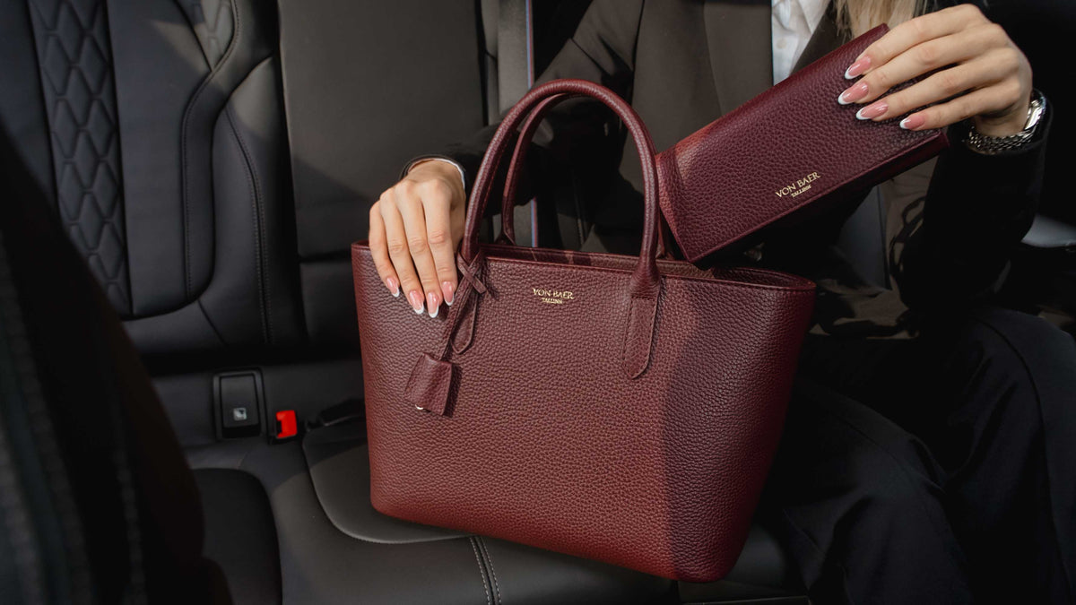 Von Baer Allure burgundy luxury RFID leather wallet shown alongside an Estelle small tote bag, held by a person inside a car for a premium lifestyle view.