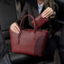 Von Baer Estelle small burgundy pebbled leather tote bag and matching Celeste zip wallet, held by a woman in a black blazer inside a car.