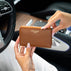 Von Baer Celeste small cognac tan full-grain leather zip-around wallet held inside a luxury Mercedes car interior, featuring gold-tone hardware and gold-embossed Von Baer Tallinn branding.
