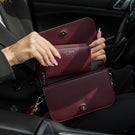 Von Baer Celeste small burgundy full-grain leather zip-around wallet demonstrated inside the Isabella small leather crossbody bag interior, held open inside a car setting with gold-tone hardware and gold-embossed Von Baer Tallinn branding.