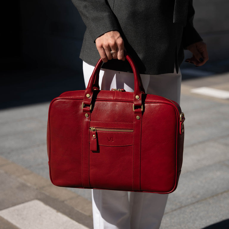 A close-up of a beautiful woman holding a red Von Baer City luxury leather laptop bag with a shoulder strap.
