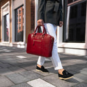 A beautiful woman in a city setting, holding a red Von Baer City luxury leather laptop bag with a shoulder strap.