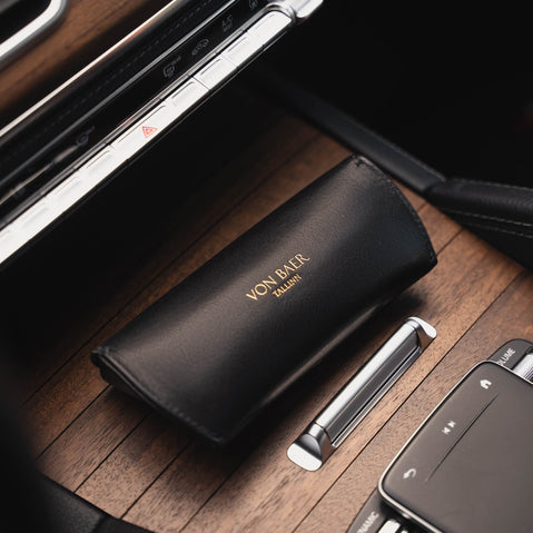 A rear-side view of a black Von Baer Deluxe luxury leather sunglasses and glasses case on a wooden panel in a car.