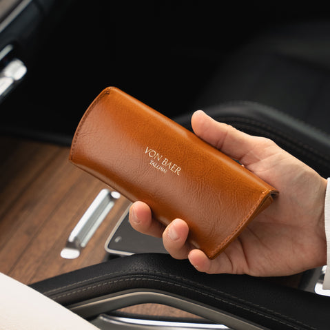 Hand holding a tan leather wallet with 'Von Baer' branding inside a car.
