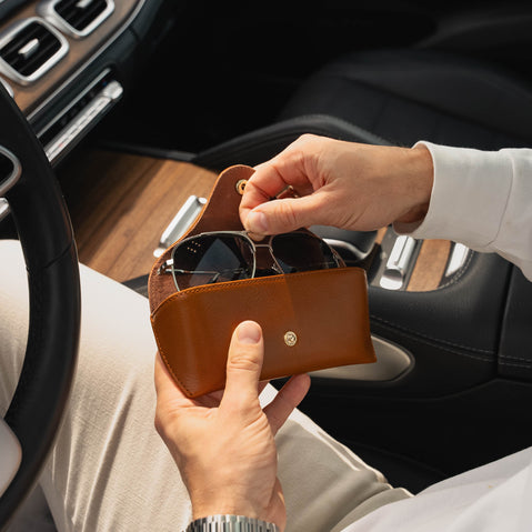 Person holding a high quality tan leather sunglasses case with sunglasses inside, sitting in a car.