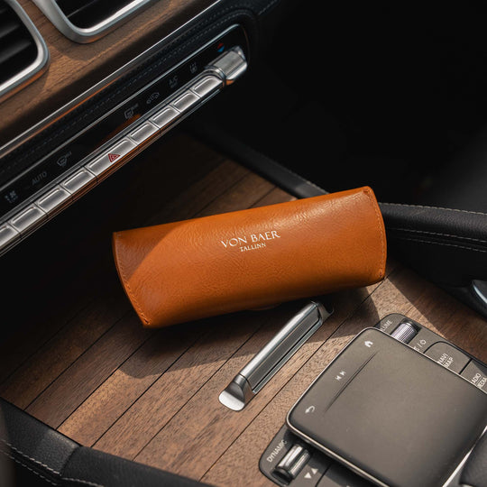 Tan Italian leather glasses case with 'Von Baer' branding on a car's wooden dashboard in mercedes