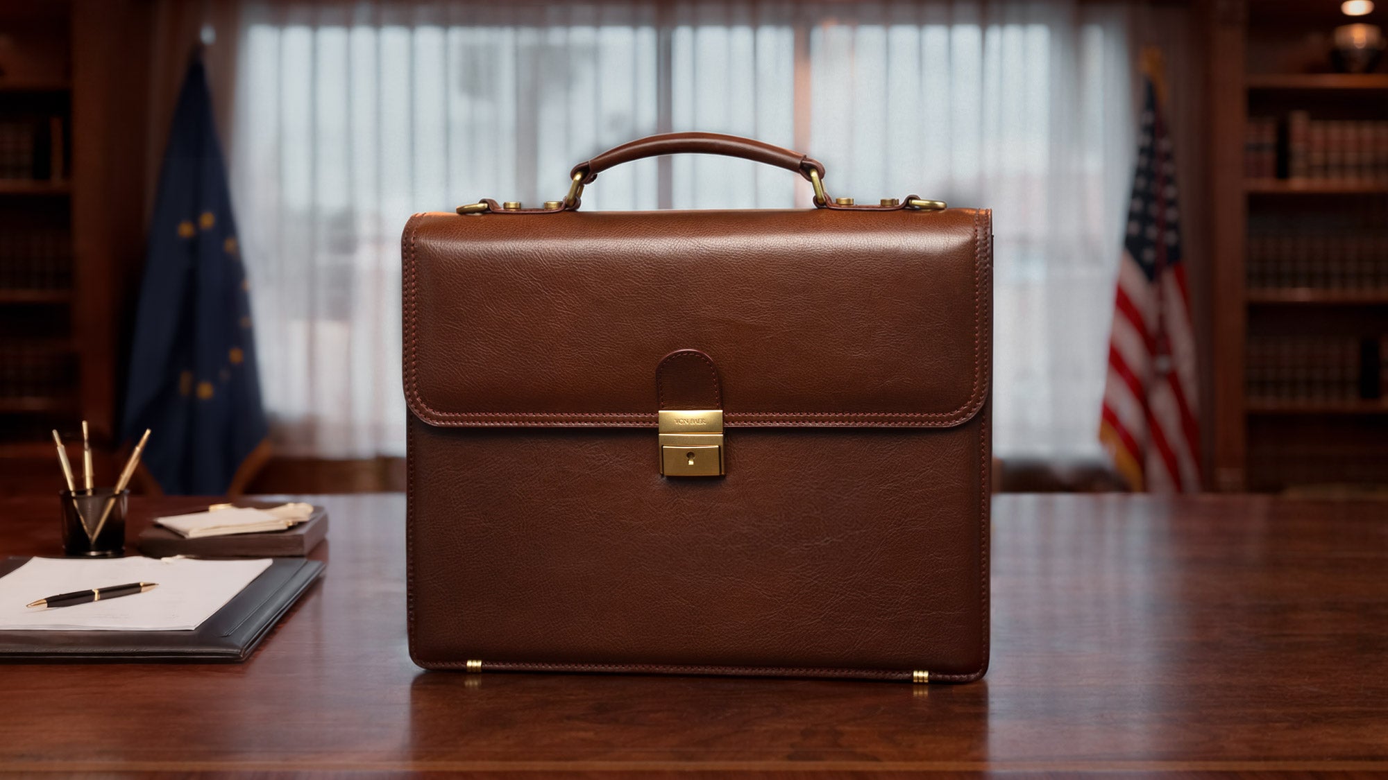 Von Baer diplomat luxurious premium brown full-grain leather men's briefcase, displayed on a desk in a luxury office with flags and books in the background, highlighting elegance and craftsmanship