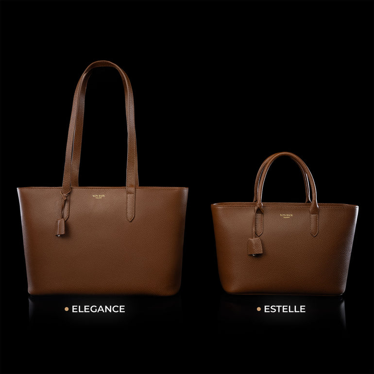 Von Baer Elegance and Estelle women's full-grain leather tote bags in cognac and tan, displayed side by side on a black background to compare sizes, featuring matching top handles, hanging leather tags, and gold-tone logo plaques, with the larger Elegance bag on the left and the smaller Estelle bag on the right
