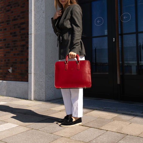 A woman is shown standing against a modern building, holding a Von Baer elegant luxury leather laptop bag.