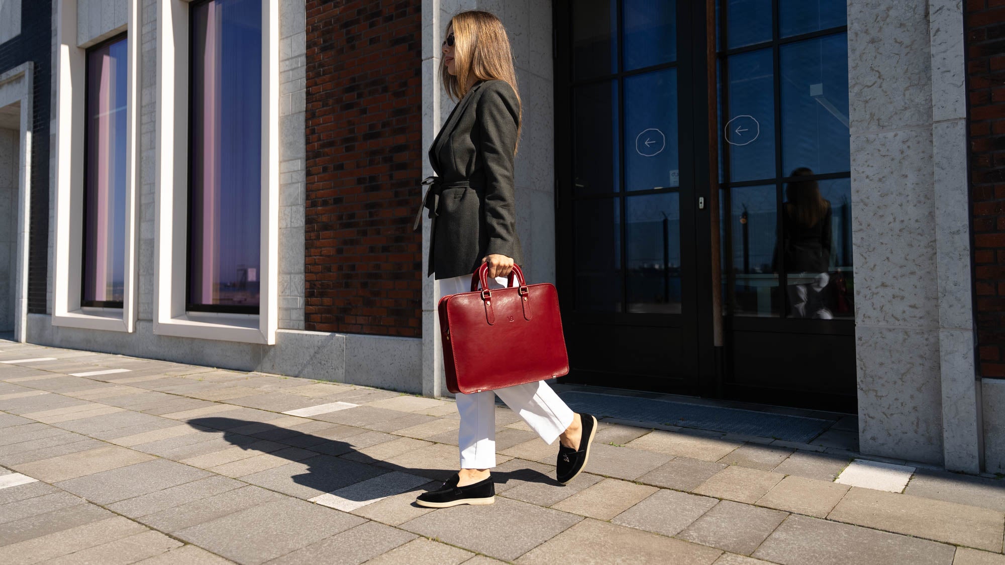 A good-looking businesswoman is carrying a red Von Baer elegant luxury leather laptop bag.