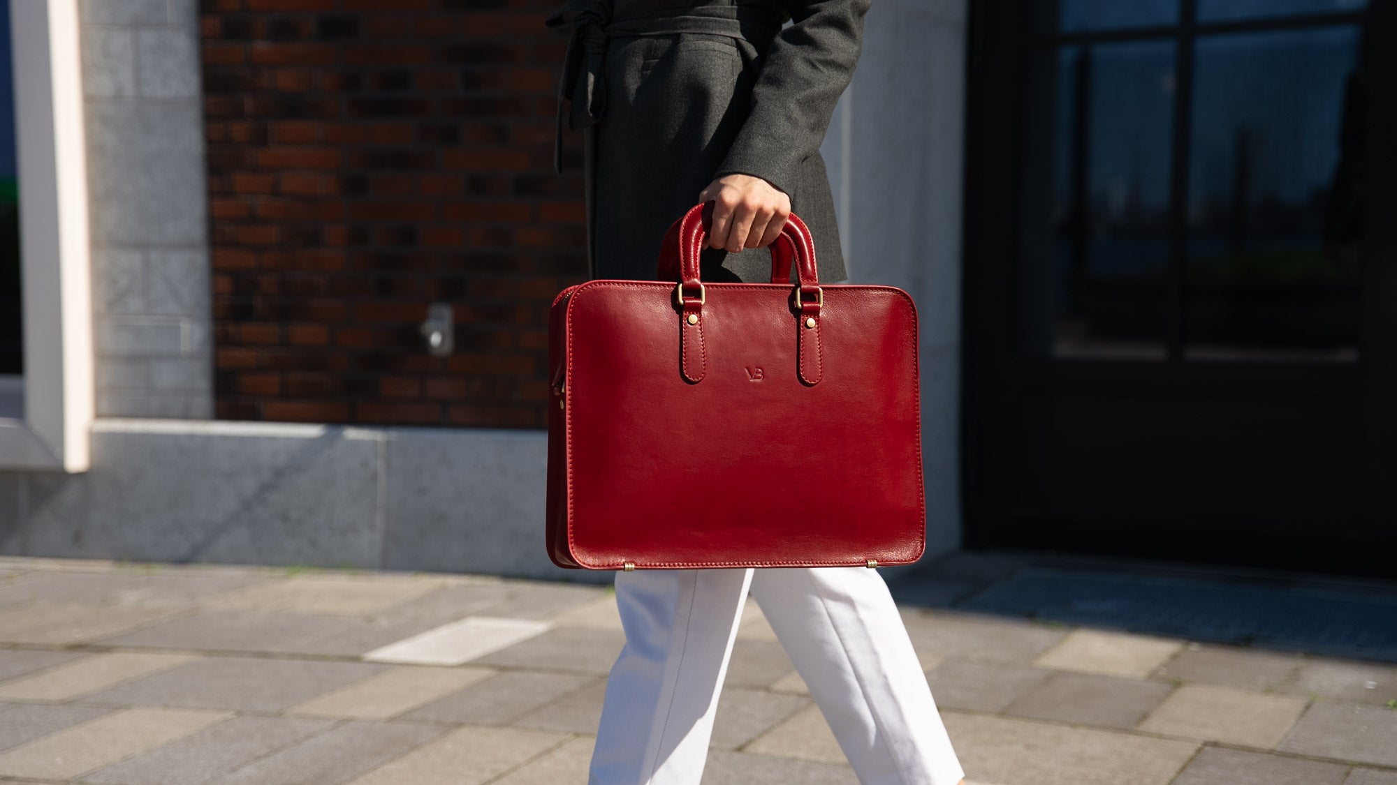A woman dressed in a casual suit holding a red Von Baer elegant luxury leather laptop bag.