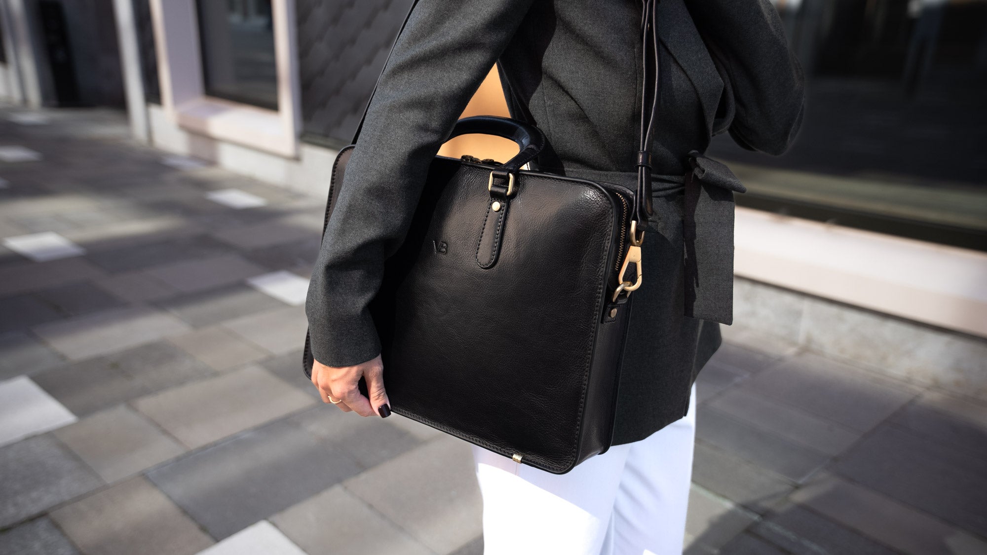 A beautiful woman holding a black Von Baer elegant luxury leather laptop bag with a shoulder strap in a city setting.