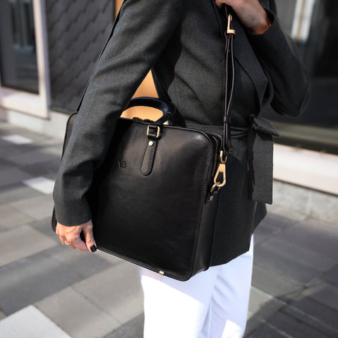 A beautiful woman in a city setting, holding a black Von Baer elegant luxury leather laptop bag with a shoulder strap.