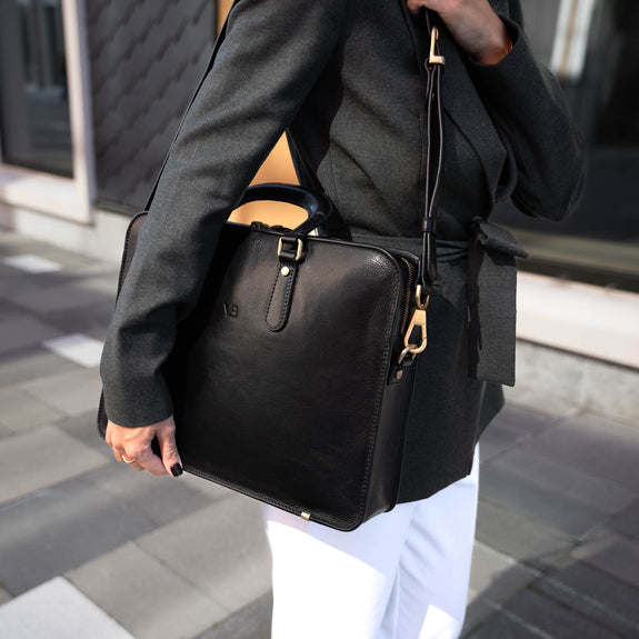 A beautiful woman in a city setting, holding a black Von Baer elegant luxury leather laptop bag with a shoulder strap.