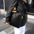 A beautiful woman in a city setting, holding a black Von Baer elegant luxury leather laptop bag with a shoulder strap.