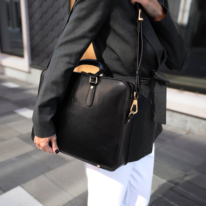 A beautiful woman in a city setting, holding a black Von Baer elegant luxury leather laptop bag with a shoulder strap.