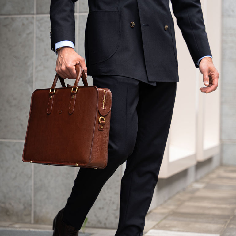 A businessman holding a brown Von Baer elegant slim leather laptop bag.