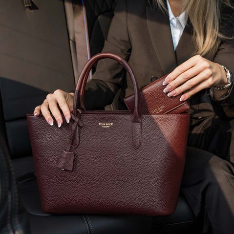 Von Baer Elise trifold wallet and Isabella small crossbody bag in cognac pebbled leather shown as a woman in a brown blazer places the matching wallet inside the bag in a car lifestyle setting.