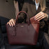 Von Baer Elise trifold wallet and Isabella small crossbody bag in cognac pebbled leather shown as a woman in a brown blazer places the matching wallet inside the bag in a car lifestyle setting.