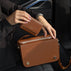 Von Baer Elise trifold wallet and Estelle small tote bag in burgundy pebbled leather shown as a person in a black blazer holds the wallet above the matching bag inside a car.