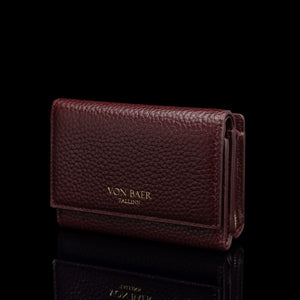 Von Baer Elise women's burgundy pebbled leather trifold wallet shown from a three-quarter front view on a reflective black surface, featuring gold-embossed Von Baer Tallinn branding.