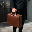 Person holding a brown leather briefcase outdoors