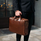 Person holding a brown leather briefcase outdoors