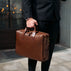 Person holding a brown leather briefcase outdoors