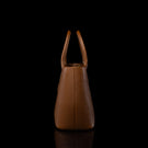 A structured brown pebbled leather handbag with double top handles, shown from the back against a solid black background with a subtle reflection below.