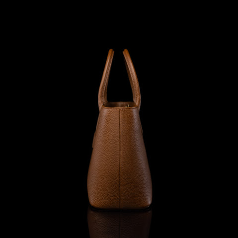 A structured brown pebbled leather handbag with double top handles, shown from the back against a solid black background with a subtle reflection below.