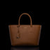 A brown pebbled leather tote bag with double top handles, a hanging leather tag, and a small gold-tone logo plaque on the front, photographed against a solid black background.