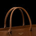 Close-up of a brown pebbled leather handbag with double top handles and a small gold-toned VON BAER logo on the front, set against a solid black background.
