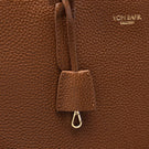Close-up of a brown pebbled leather bag with a hanging leather tab and metal clasp, featuring the gold-toned embossed brand name VON BAER on the upper right.