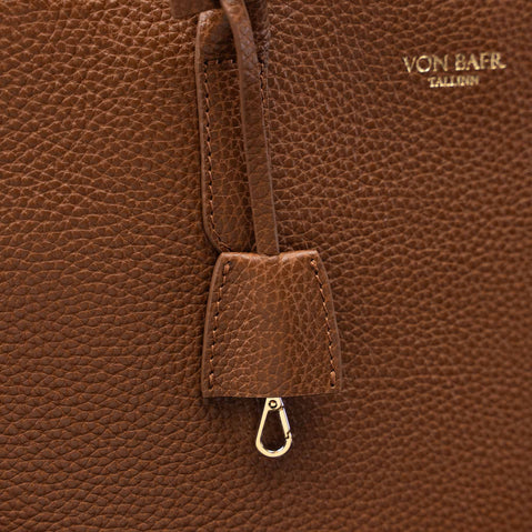 Close-up of a brown pebbled leather bag with a hanging leather tab and metal clasp, featuring the gold-toned embossed brand name VON BAER on the upper right.