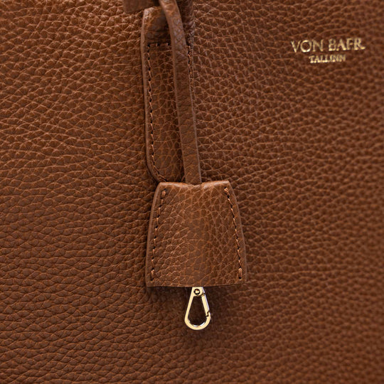 Close-up of a brown pebbled leather bag with a hanging leather tab and metal clasp, featuring the gold-toned embossed brand name VON BAER on the upper right.