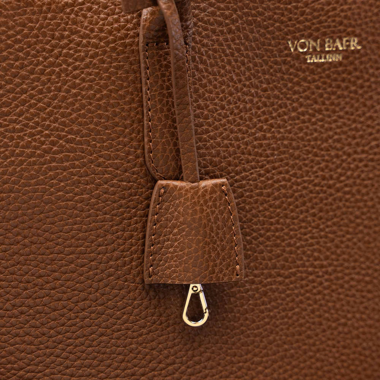 Close-up of a brown pebbled leather bag with a hanging leather tab and metal clasp, featuring the gold-toned embossed brand name VON BAER on the upper right.