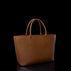 A structured tan leather tote bag with a pebbled texture and double top handles, photographed against a solid black background with a subtle reflection below.