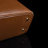 Close-up of a brown pebbled leather bag corner with two small gold-tone metal studs on a black background.