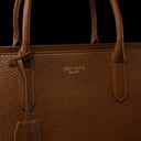 Close-up of a brown pebbled leather tote bag with gold-toned 'VON BAER' branding on the front, set against a solid black background.