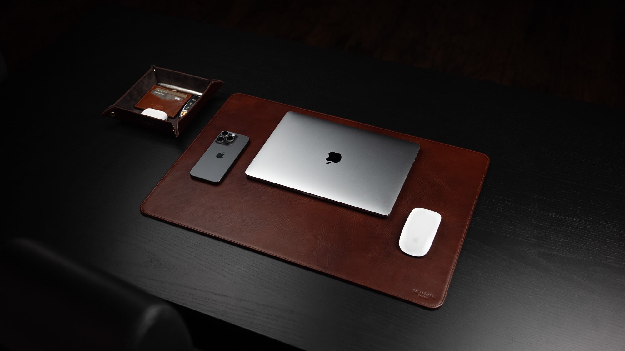 Von Baer executive luxury leather desk pad in brown on dark wood table with MacBook, iPhone, mouse, and tray.