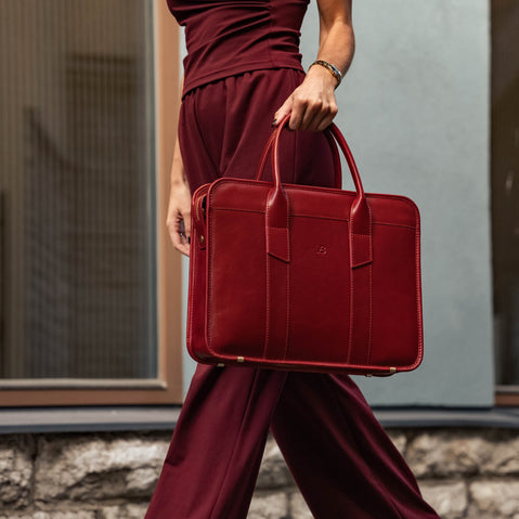 A woman walking against a blue wall, holding a red Von Baer exquisite luxury leather laptop bag.