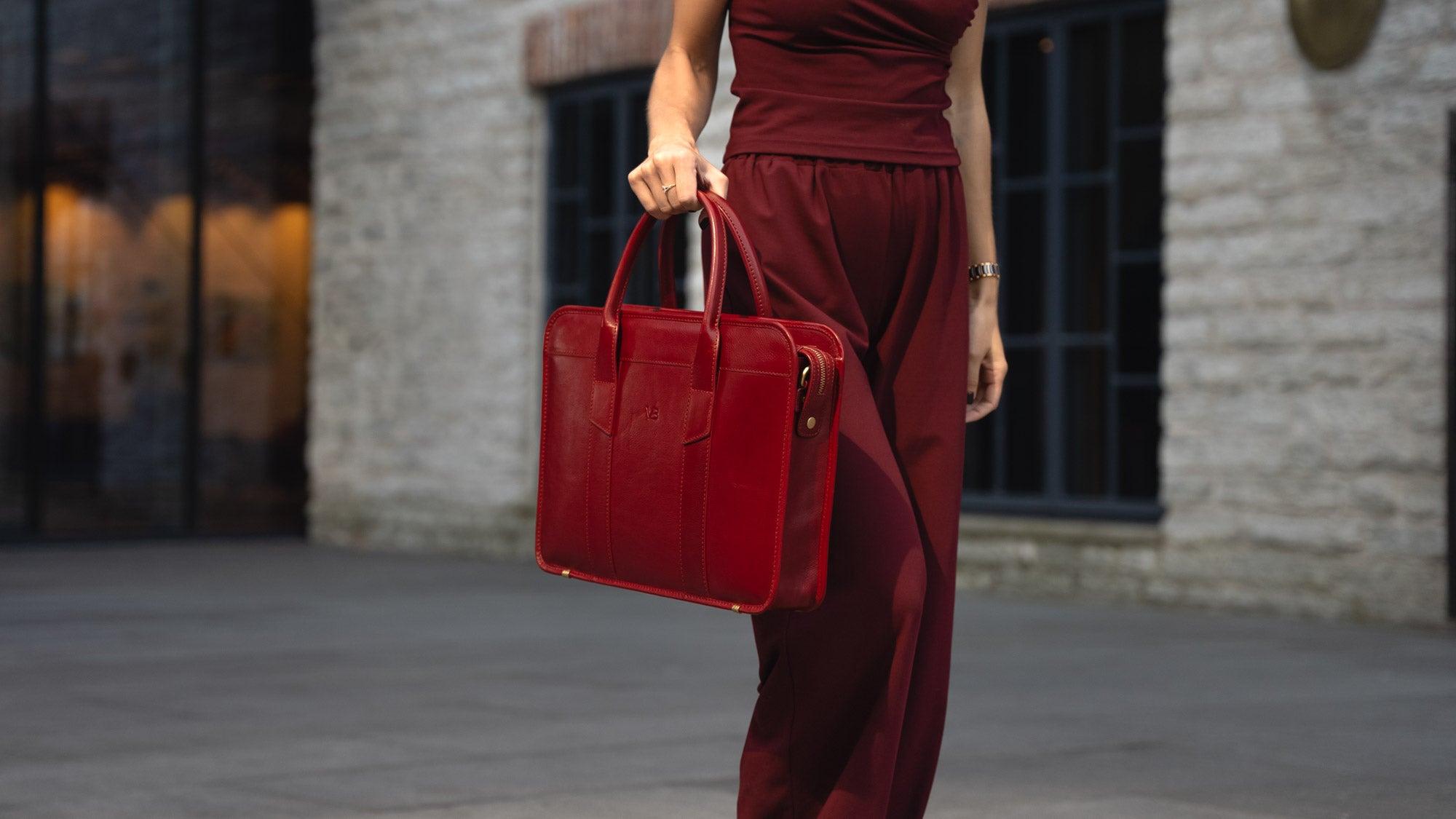 A woman walking in a city, holding a red Von Baer exquisite luxury leather laptop bag.