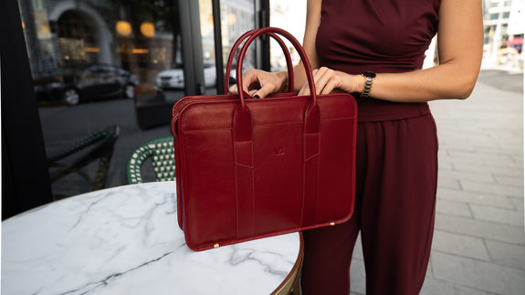 A female model is shown with a red Von Baer exquisite luxury leather laptop bag for women, which is placed on a marble table.