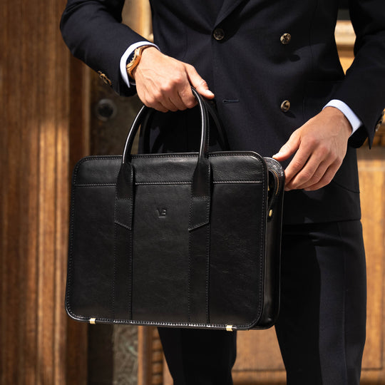 An exquisite, slim, black Von Baer full-grain leather laptop briefcase for business travel, held by a man.